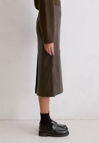 Brauner Leder-Midirock mit Seitenschlitzen und glatter Textur. Kombiniert mit schwarzen Loafers und knielangen Socken.