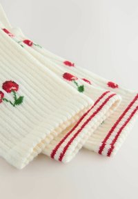 Ribbad krämfärgad stickad tyg med röd rosbroderi och gröna stjälkar, accentuerad med rödrandiga muddar. Strukturerad och mjuk känsla.
