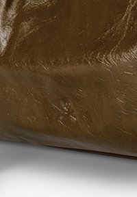 Hnědá kožená textura s hladkým, lesklým povrchem, která vykazuje jemné vrásky a malou prohlubeň blízko středu.