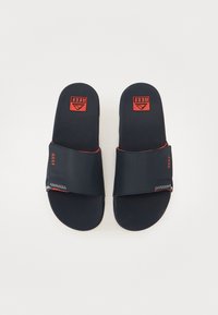 Námorné gumové šľapky s širokým remienkom, červeným logom "REEF", textúrovanou stielkou a bielym prešitým akcentom.