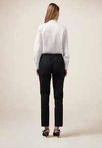 Bílá blůza s dlouhými rukávy v kombinaci s černými kalhotami s elastickým pasem, doplněná černými lodičkami s mašlovými akcenty.