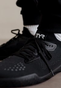 Svarte treningssko med teksturert mesh-overdel, minimalistisk design og TYR-merke på kragen, med svarte lisser og detaljer.