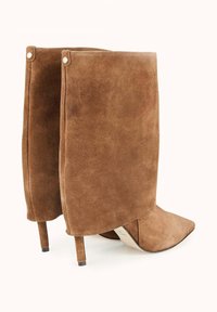 Bottines en suède marron avec un orteil pointu et un talon stiletto de hauteur moyenne, présentant une texture lisse et mate ainsi que des coutures décoratives subtiles.