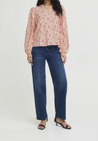 Blouse à manches longues florale avec un décolleté en V dans des tons de rose et de rouge, associée à un jean large bleu et des sandales à talons noires.