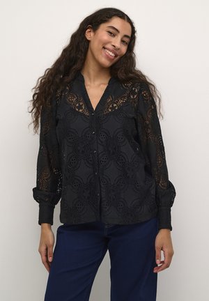 Black lace blouse featuring floral embroidery patterns, long sleeves with button cuffs, and a notch collar, paired with blue denim pants.