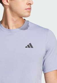 Lichtpaarse sport t-shirt met een ronde hals. Bevat een zwart Adidas-logo op de borst. Zachte stof met een gladde textuur.