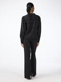 Black, embroidered long-sleeve blouse with a collared neck; paired with black, fitted trousers featuring side slits at the hem.