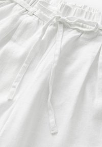 Pantaloni corti bianchi in lino con vita elastica e lacci, realizzati in un tessuto morbido e testurizzato, dal taglio rilassato. Senza motivi o accenti visibili.