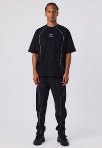 Zwarte oversized t-shirt en broek set met blauwe contrasterende stiksels. T-shirt heeft korte mouwen en een ronde halslijn. Tekstlogo op de borst.