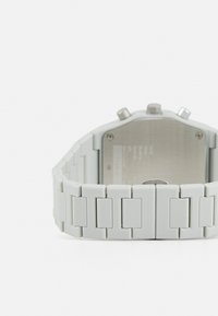 Montre en silicone gris avec un bracelet à maillons. Comprend un fond en acier inoxydable argenté et trois boutons sur le côté du boîtier.