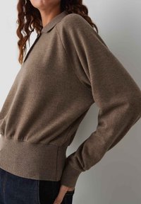 Brązowy sweter wykonany z miękkiego materiału z kołnierzykiem, ribbowanymi mankietami i dołem, o luźnym kroju i lekko teksturowanej powierzchni.