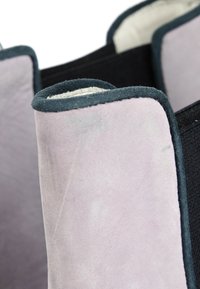 Gros plan d'une attelle protectrice en daim beige avec bordure noire et sangles élastiques conçue pour le soutien des articulations.