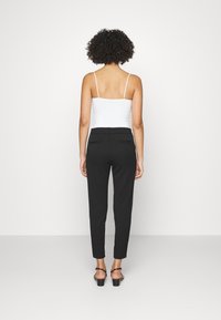 Pantalons noirs fuselés avec une texture lisse, dotés d'une taille élastiquée et de deux poches arrière, associés à un haut blanc à fines bretelles.