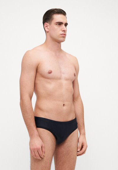 Caleçons de bain noirs avec une texture lisse, présentant un design taille basse et une ceinture simple, présentés sur un modèle dans un fond neutre.