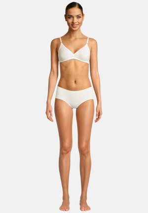 Giovane donna in piedi a piedi nudi che indossa un reggiseno bianco e slip bianchi senza cuciture abbinati su uno sfondo semplice.