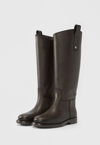 Ψηλές μαύρες δερμάτινες μπότες με ομαλή υφή. Διαθέτουν στρογγυλεμένη μύτη, μινιμαλιστικό σχέδιο και μια μικρή λεπτομέρεια με θηλιά στην κορυφή.