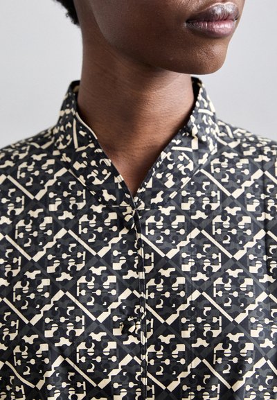 Musthave mustariburu must urbana kampshirt, kus puhas sarnane vitraal mustriga, millel on mandariinikaelus ja nööbid.