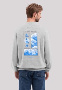 Grauer Sweatshirt mit einem blauen Wellen-Graphic und dem Text "Shibui Series" auf dem Rücken. Rippbündchen, lockere Passform, weiche Stofftextur.
