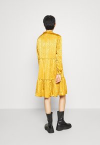 Žluté dlouhé šaty s texturovaným vzorem a volánkovým lemem. Doplnené černými kotníkovými botami, vytvářející uvolněný střih.