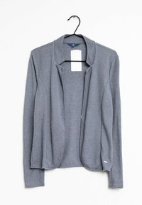 Cardigan grigio aperto in maglia con maniche lunghe appeso a un appendiabiti nero su sfondo bianco, con etichetta del prezzo bianca e vuota.