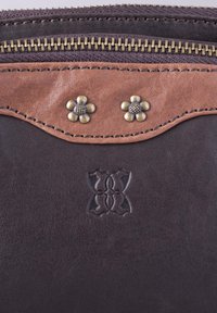 Brown leather accessory with a darker bottom, featuring a decorative tan panel, two brass flower accents, and embossed detailing.
