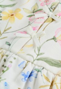 Kerge valge lillemustriga kangas, kus on kollased, roosad ja sinised lilled; sisaldab väikeseid valgeid paelu ja volditud detaile heml.