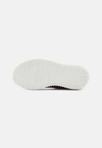 Shoe sole featuring a textured white rubber design with ridges and a slight curve, accompanied by embossed brand details in an understated font.