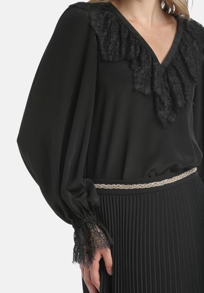Black blouse with lace-frilled V-neck, billowy sleeves, and lace cuffs. Paired with pleated black skirt featuring a beaded waistband.
