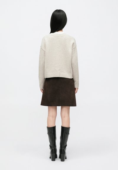 Camisola bege de malha com bainha canelada combinada com saia de camurça escura. A modelo usa botas altas de couro preto. Design simples e elegante.