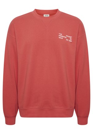 Korálová mikina se skládacím výstřihem a žebrovanými manžetami. Obsahuje bílý text: "THE ARCHIVE" prezentováno značkou SOLID, založena v roce 1999. Měkká tkanina.