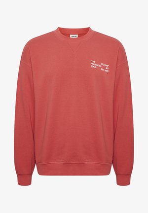 Korala dukserica s okruglim izrezom i rebrastim manžetama. Sadrži bijeli natpis: "THE ARCHIVE" predstavljen od strane SOLID, osnovan 1999. Mekani materijal.