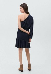 Morsko modra obleka z enim ramenom, prilegajoč top, obrobljen rob, mehak material, drapirana rokav, do kolen, v kombinaciji s svetlo rjavimi gležnjači.