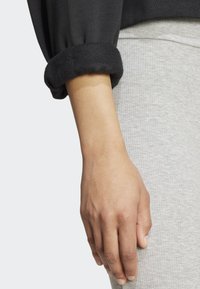 Černá mikina s ohrnutými fleecovými manžetami, vystavená vedle světle šedé ribované látky. Zaměření na ruku položenou na oblečení.