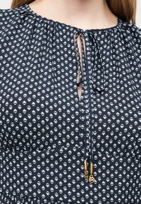 Στολή ναυτικού με λευκό ανθισμένο μοτίβο, λαιμόκοψη με άνοιγμα που δένεται με λεπτές κορδέλες τελειώνοντας σε χρυσά μοτίφ MK.