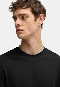 T-shirt nera a girocollo con una texture liscia e opaca. Design slim fit, maniche corte e dettagli minimi su sfondo uniforme.