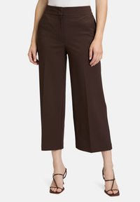 Pantalons larges marron en tissu doux avec une texture lisse. Dotés d'une taille haute et de poches latérales. Assortis à des sandales à lanières.