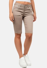Shorts beiges à mi-cuisse avec une texture lisse, présentant des coutures de couleur claire, deux poches à l'avant, et portés avec des baskets blanches.