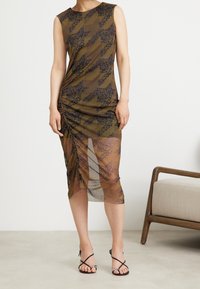 Vestido sin mangas en marrón con patrones florales y geométricos en negro. Presenta detalles fruncidos en los laterales y una sección inferior transparente.