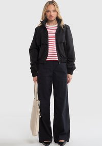 Black cropped jacket with elastic cuffs, striped red and white shirt, wide-leg dark pants, and a beige tote bag. Smooth fabric textures.