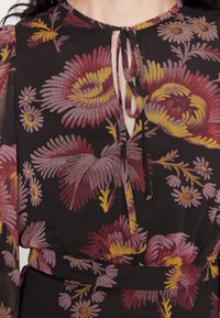 Musta kukkakuvioinen paita, jossa on vaaleanpunaisia ja keltaisia kuvioita, kevyt kangas, pyöreä pääntie, edessä solmittava yksityiskohta ja puffihihat.