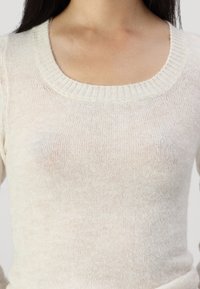 Suéter de punto de un beige claro, con un amplio escote acanalado. La tela parece suave y ligeramente translúcida, mostrando una textura delicada.