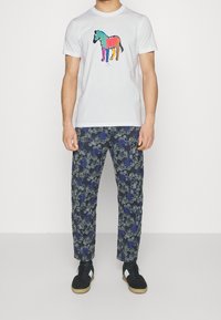 Biała koszulka z kolorową grafiką konia, połączona z granatowymi spodniami w rozbudowany wzór w niebieskie i szare kwiaty. Czarne sneakersy.