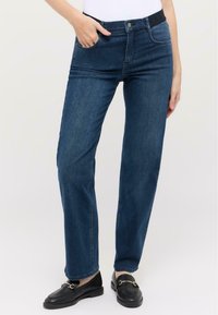 Jeans din denim de un albastru închis cu un design cu picior drept, buzunare frontale și un talie neagră. Purtați cu mocasini negri.