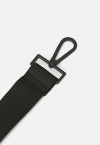 Sangle en nylon noir avec une boucle en plastique rectangulaire et un clip. La sangle présente une texture lisse et des coutures sécurisées.