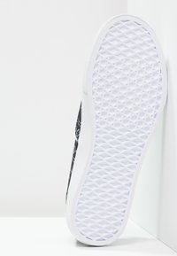 Baskets noires avec tige en tissu à motifs, semelle en caoutchouc blanc texturé et accents lisses. Présente un design à profil bas et des panneaux latéraux élastiques.