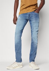 Ljusblå jeans i denim med en rak passform, med blekta partier och kontrastsömmar, kombinerade med sneakers i krämfärg.