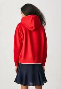 Felpa rossa in cotone con cappuccio, polsini e parte inferiore a costine, abbinata a una gonna svasata blu navy. Tessuto liscio e design informale.