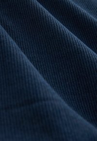 Tessuto blu scuro con una fine trama a righe verticali e morbide pieghe che creano ombre diagonali sulla superficie.