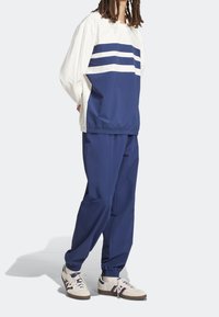 Námořnický track suit s bílými pruhy přes hruď a rukávy; elastické manžety a pás; spárováno s bílými teniskami s barevnými akcenty.