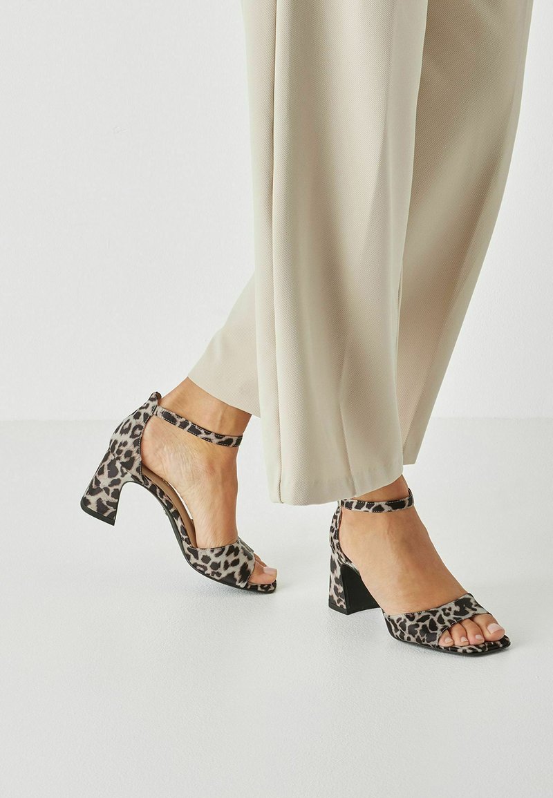 Sandales à talons hauts imprimé léopard avec une bride à la cheville, un bout ouvert, et un talon épais, fabriquées en tissu texturé aux tons neutres.